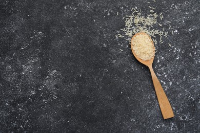 Spoon with raw rice on black textured table, top view. Space for text