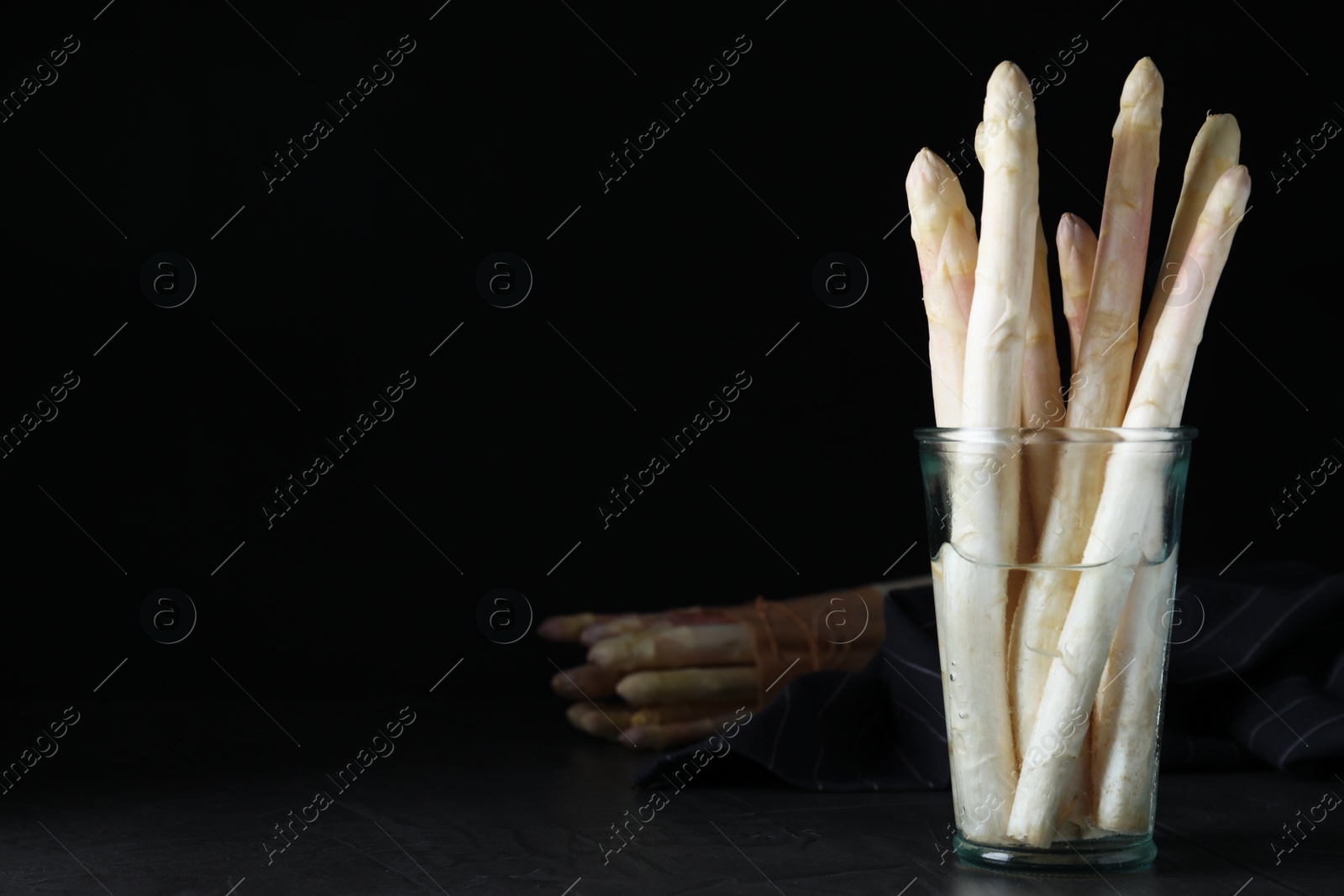 Photo of Fresh white asparagus in glass on table against black background. Space for text