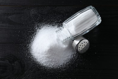 Photo of Organic salt in glass shaker on black wooden table, top view