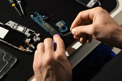 Technician repairing broken smartphone at table, closeup