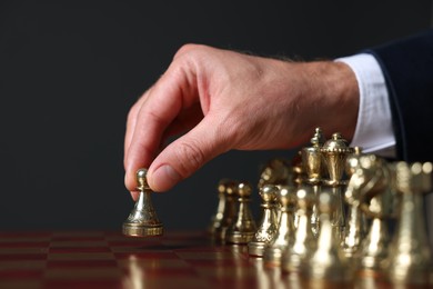 Man with game piece playing chess at board against dark background, closeup