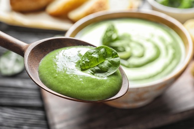 Photo of Spoon with fresh vegetable detox soup made of spinach on blurred background, closeup