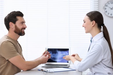 Photo of Doctor showing patient X-ray picture and educational model of dental implant in clinic
