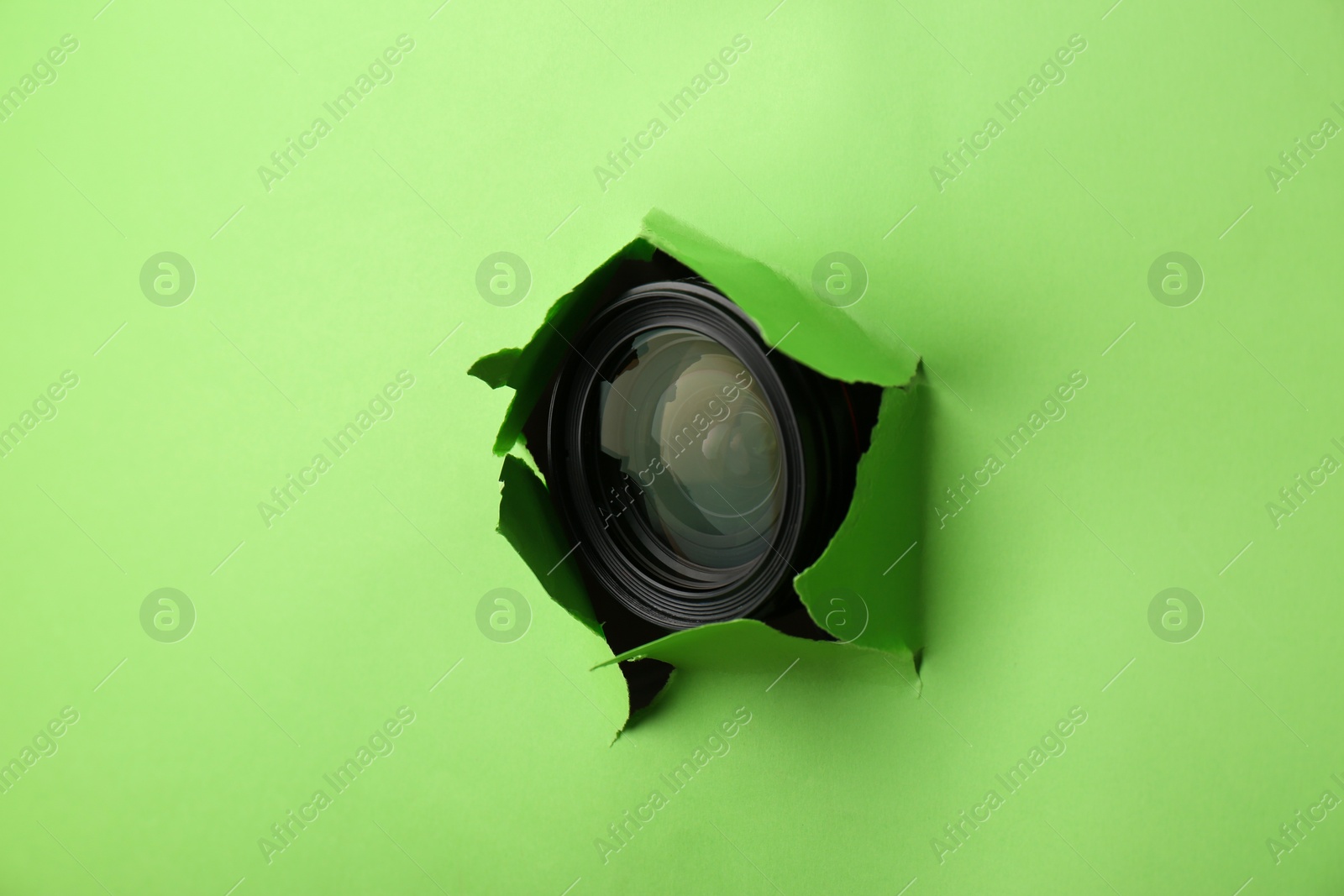 Photo of Hidden camera lens through torn hole in green paper