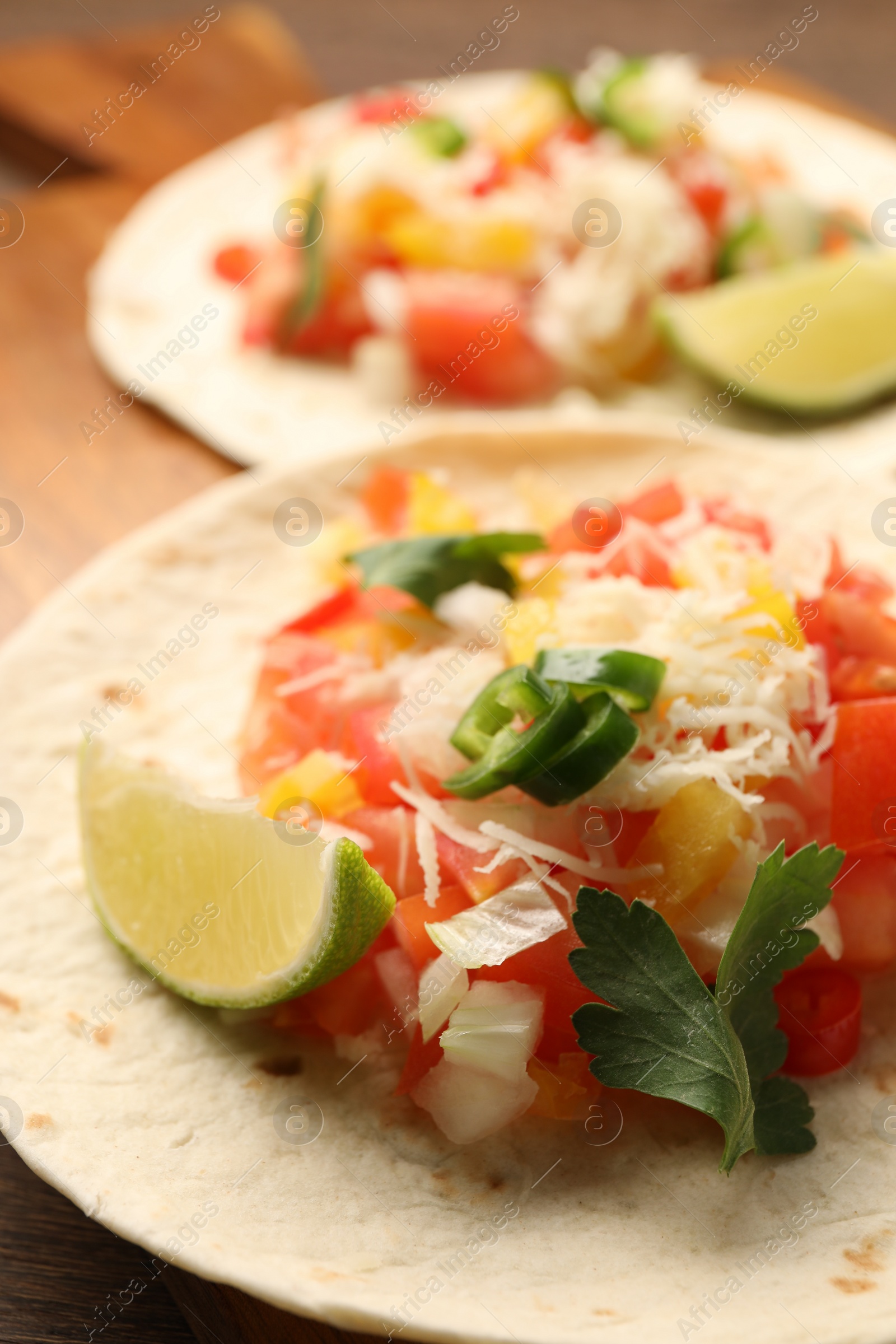 Photo of Delicious tacos with vegetables, lime and parsley on table, closeup