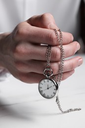 Photo of Man holding chain with elegant pocket watch at white table, closeup