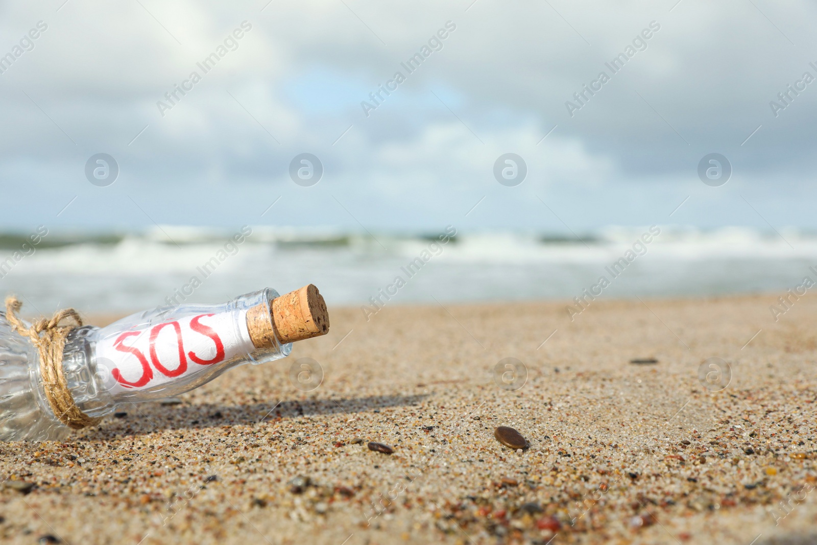 Photo of Glass bottle with SOS message on sand near sea, space for text