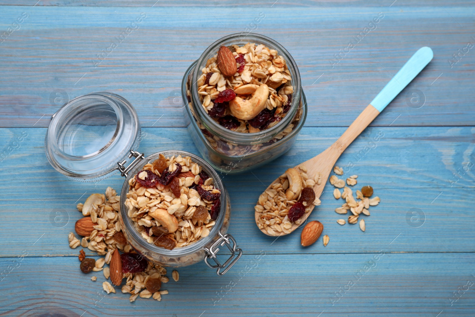 Photo of Jars of tasty granola with nuts and dry fruits on light blue wooden table, flat lay
