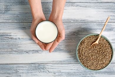 Photo of Woman holding glass of hemp milk over wooden table, top view