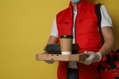 Photo of Courier in protective gloves holding order on yellow background, closeup. Food delivery service during coronavirus quarantine