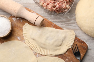Photo of Raw chebureki with tasty filling and fork on wooden table, flat lay