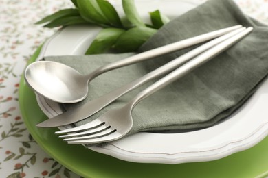 Stylish setting with cutlery, plates, napkin and floral decor on table, closeup