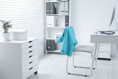 Photo of Turquoise medical uniform hanging on chair in clinic