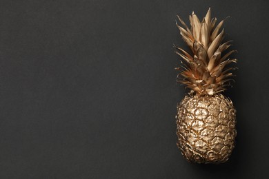 Photo of Golden pineapple on black table, top view. Space for text