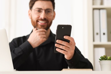 Smiling man using smartphone in office, selective focus