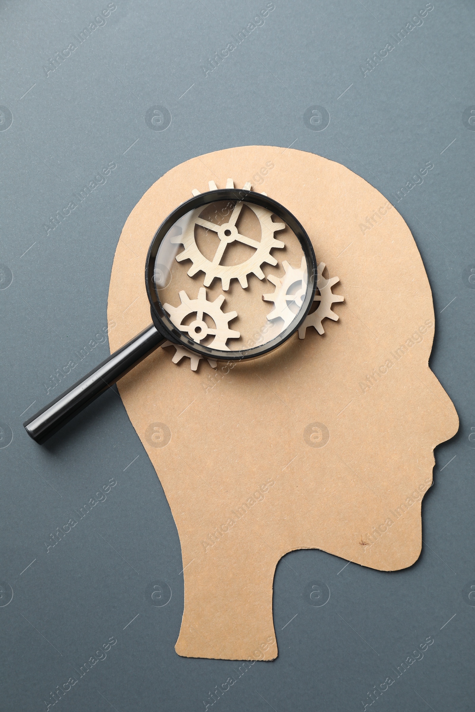 Photo of Amnesia. Human head cutout, cogwheels and magnifying glass on grey background, top view