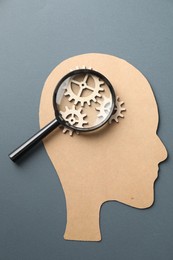 Amnesia. Human head cutout, cogwheels and magnifying glass on grey background, top view