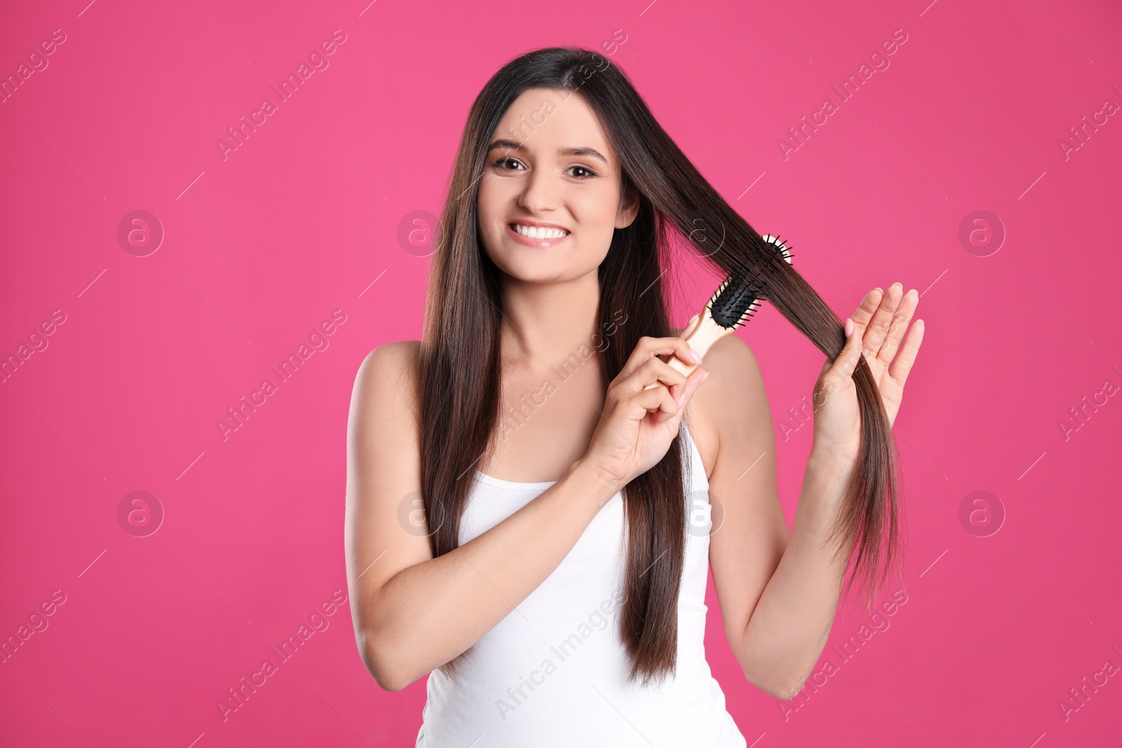 Photo of Beautiful smiling young woman with hair brush on color background