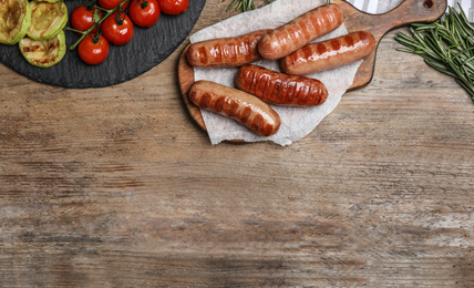 Photo of Tasty grilled sausages served on wooden table, flat lay. Space for text