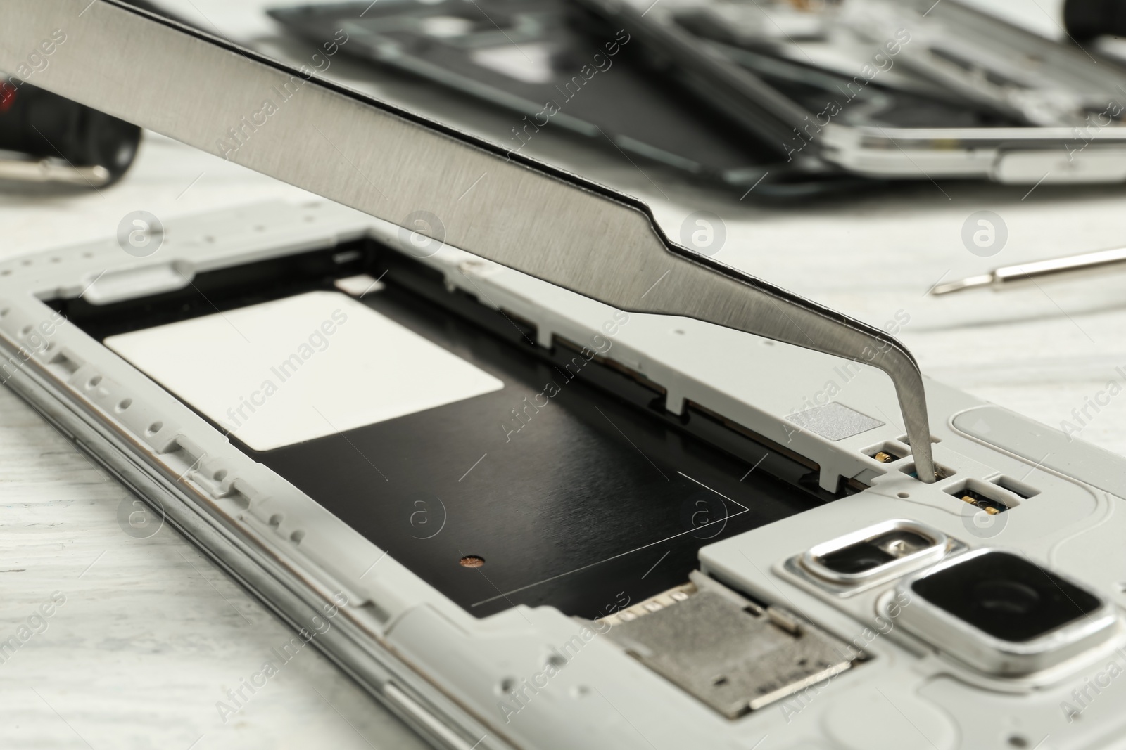 Photo of Repairing damaged smartphone with forceps at white wooden table, closeup