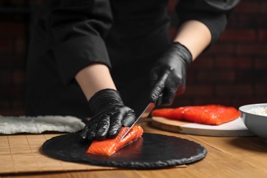 Chef in gloves cutting salmon for sushi at wooden table, closeup