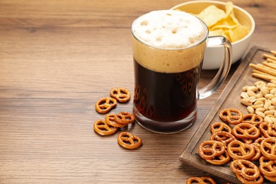 Photo of Glass of beer served with delicious pretzel crackers and other snacks on wooden table, space for text