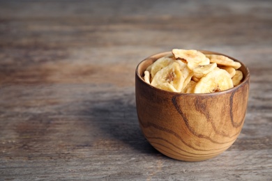 Bowl with sweet banana slices on wooden  table, space for text. Dried fruit as healthy snack