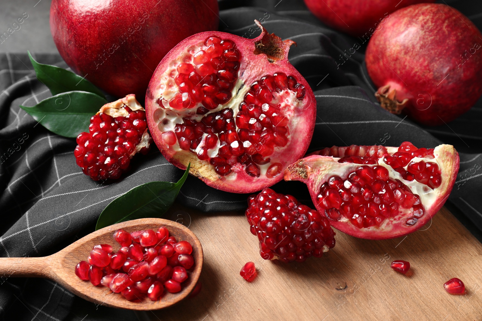 Photo of Ripe pomegranates and spoon with seeds on wooden board