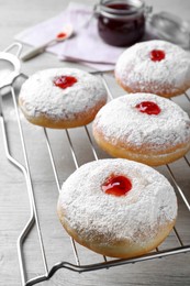Photo of Many delicious donuts with jelly and powdered sugar on cooling rack
