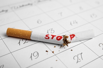 Photo of Broken cigarette with word Stop on calendar sheet. Quitting smoking concept