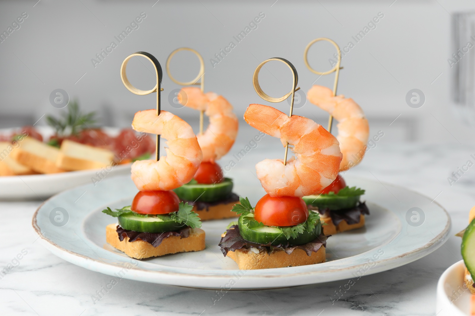 Photo of Tasty canapes with shrimps, cucumber, greens and tomatoes on white marble table, closeup