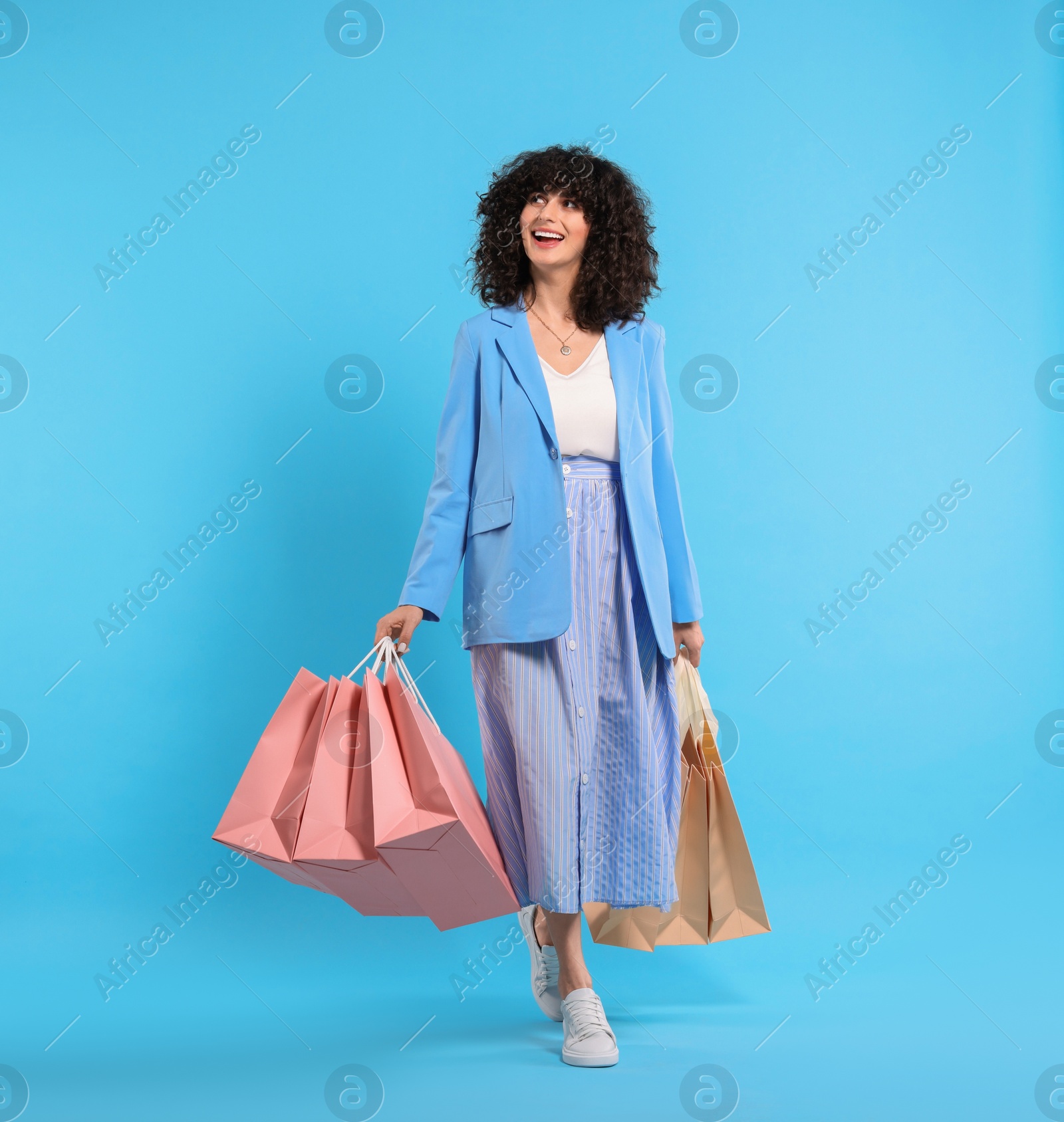 Photo of Happy young woman with shopping bags on light blue background