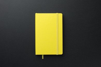 Closed yellow notebook on black background, top view