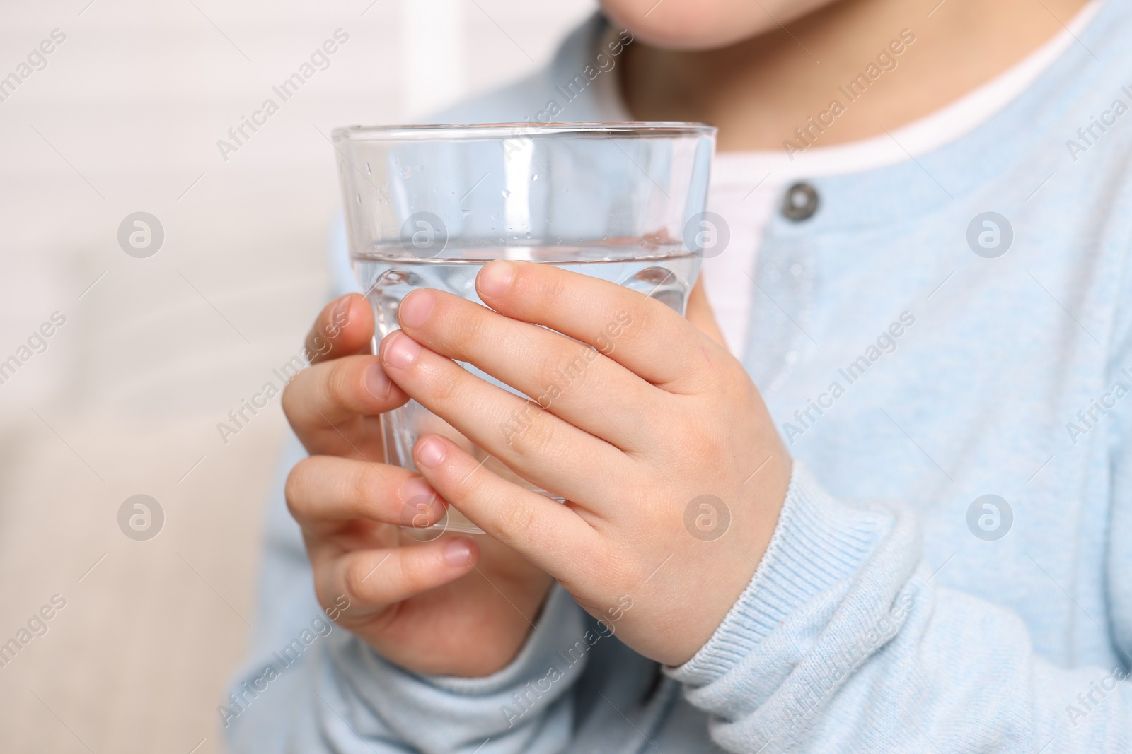 Photo of Little girl holding glass of fresh water indoors, closeup