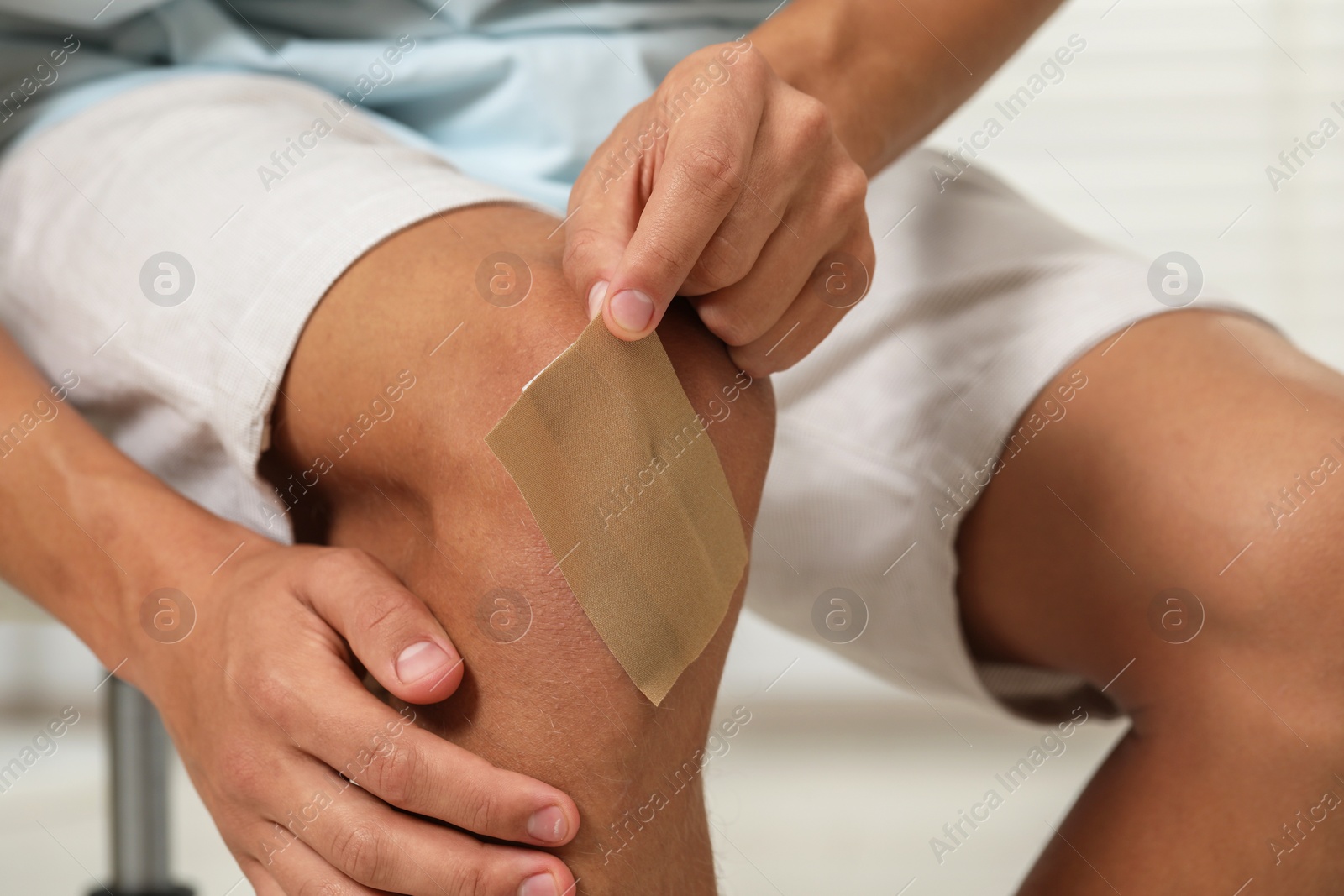 Photo of Man putting sticking plaster onto knee indoors, closeup