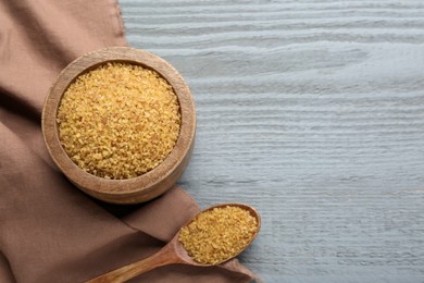 Bowl and spoon with uncooked bulgur on grey wooden table, top view. Space for text