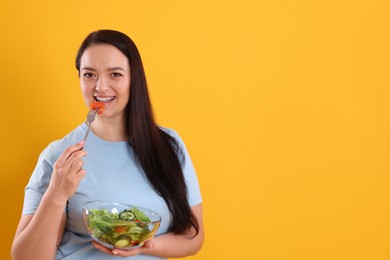 Photo of Beautiful overweight woman eating salad on yellow background, space for text. Healthy diet