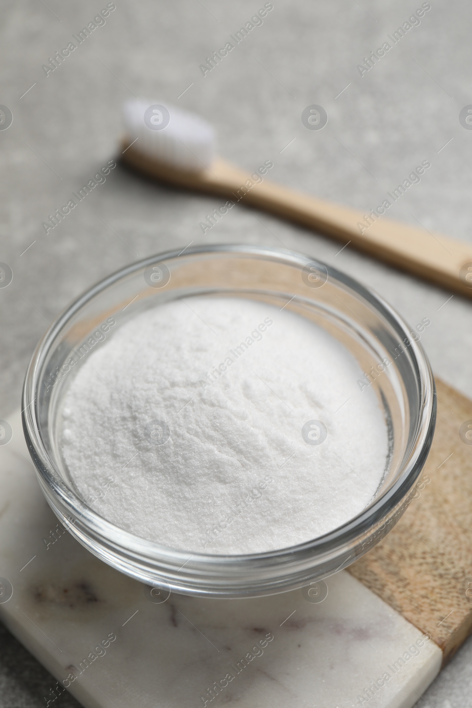 Photo of Bamboo toothbrush and bowl of baking soda on grey table, closeup