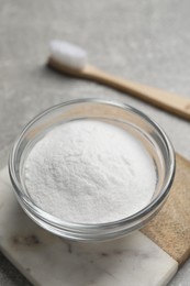 Bamboo toothbrush and bowl of baking soda on grey table, closeup