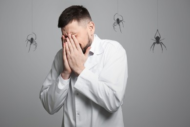 Image of Scared man suffering from panic attack on grey background. Shadows of spiders symbolizing fear and anxiety