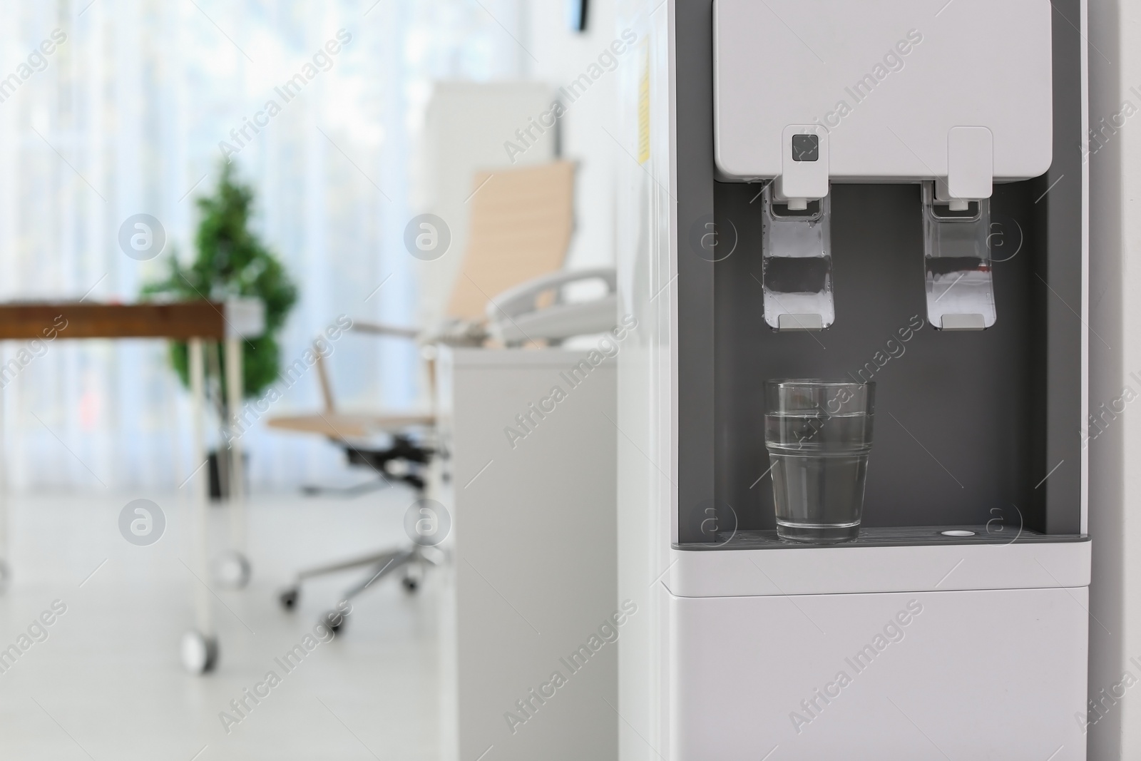 Photo of Modern water cooler with glass in office. Space for text
