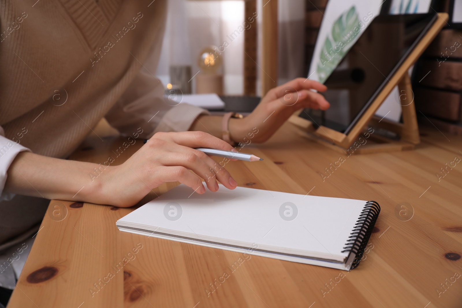 Photo of Woman drawing in sketchbook with pencil at wooden table indoors, closeup