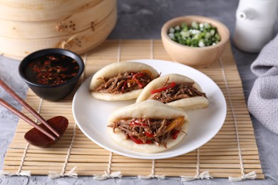 Photo of Delicious gua bao (pork belly buns), chopsticks and sauce on grey textured table, closeup