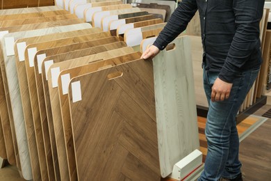 Photo of Man choosing wooden flooring among different samples in shop, closeup