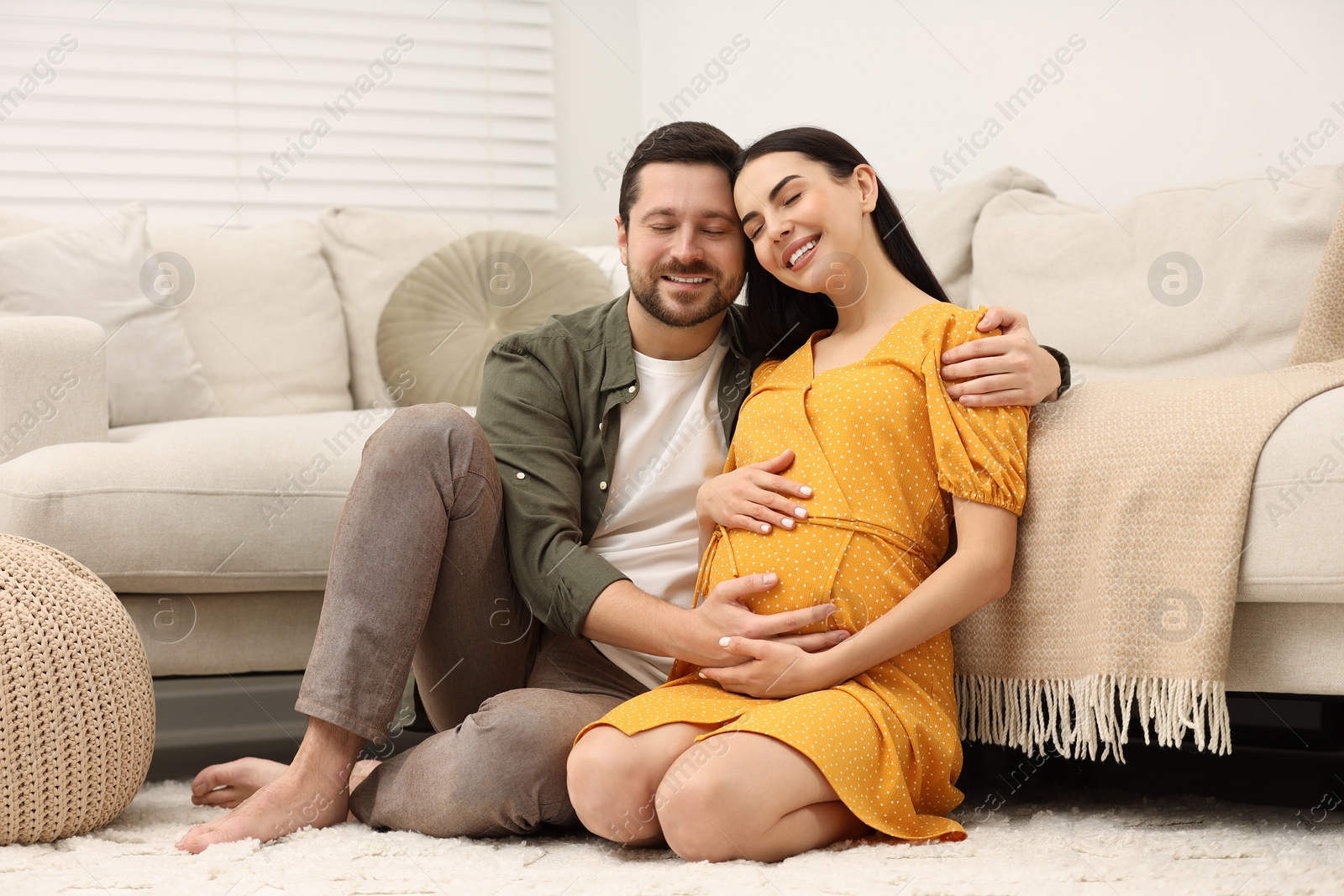 Photo of Happy pregnant woman with her husband on soft carpet at home