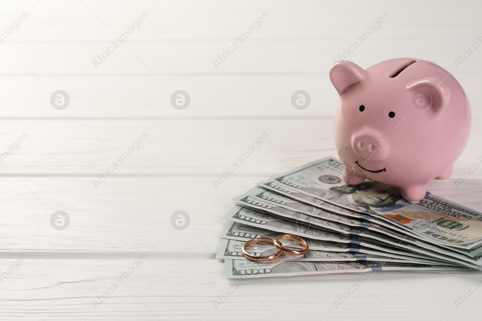 Photo of Honeymoon concept. Piggy bank, dollar banknotes and golden rings on white wooden table, closeup