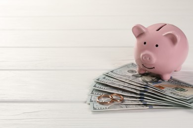 Honeymoon concept. Piggy bank, dollar banknotes and golden rings on white wooden table, closeup