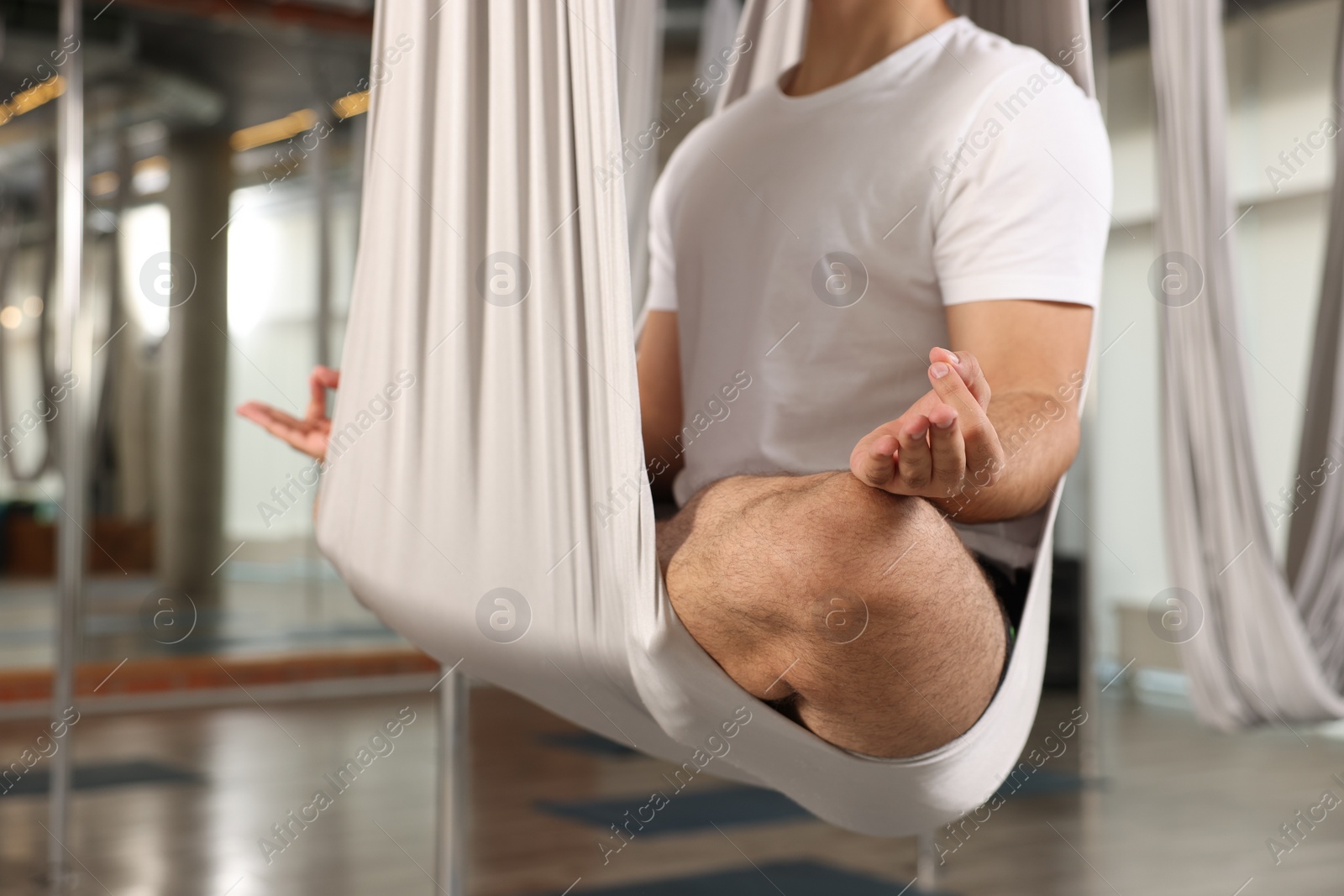 Photo of Man meditating in fly yoga hammock indoors, closeup