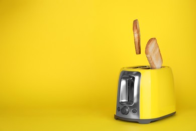 Photo of Bread slices popping up out of electric toaster on yellow background. Space for text