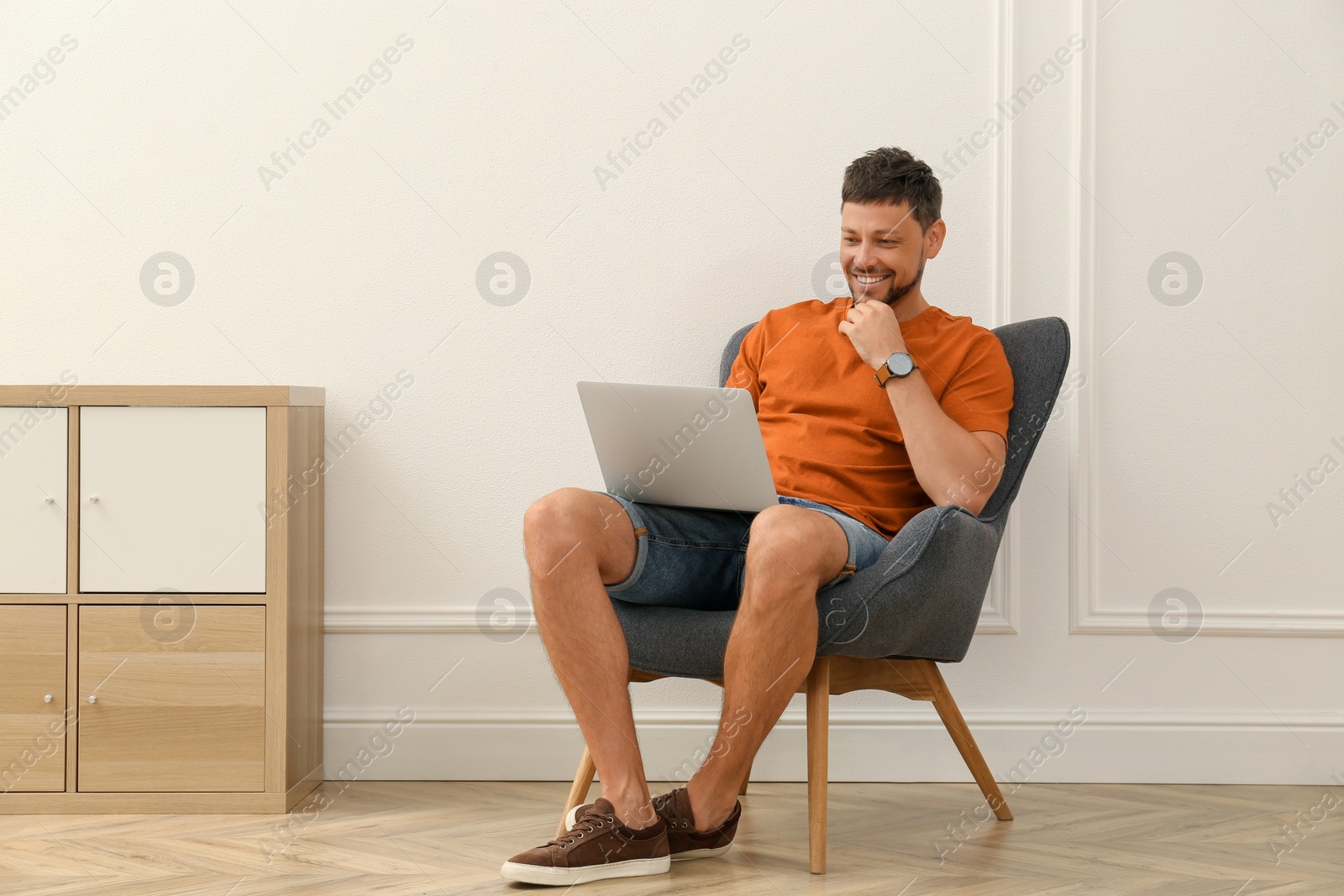 Photo of Happy man using laptop in armchair at home. Internet shopping